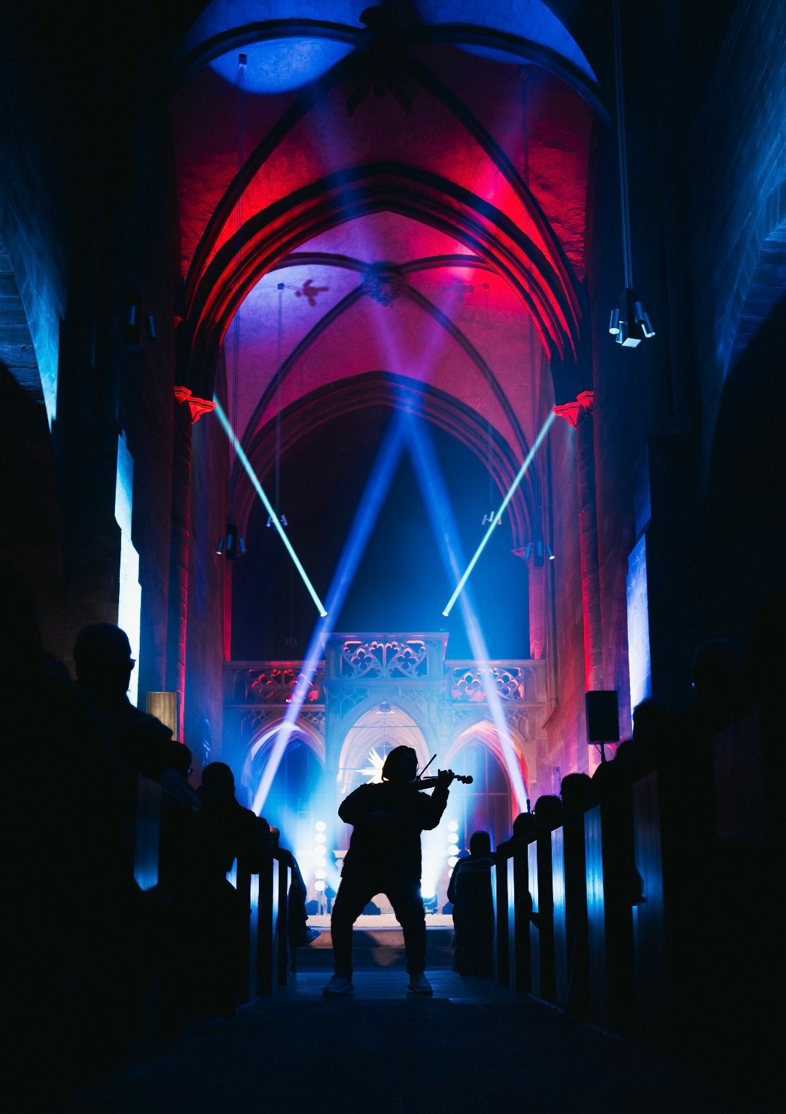 Churching Violin: Noah Leonne im Mittelgang einer Kirche, Lichtshow in Rot und Blau